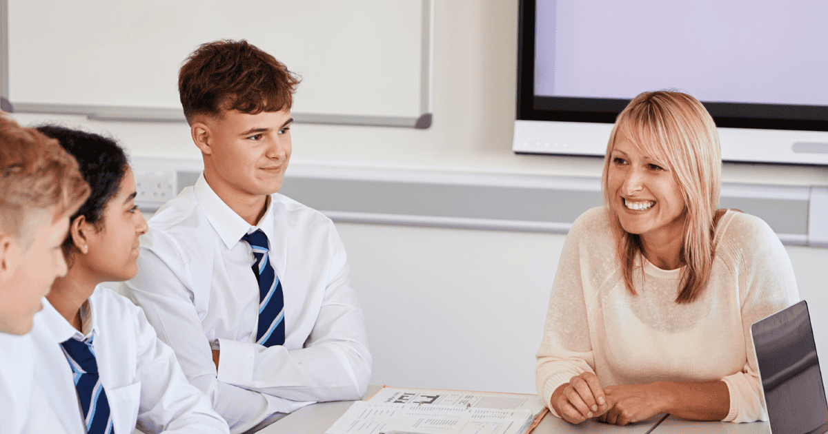 A female teacher smiling with 3 teen students around a work table