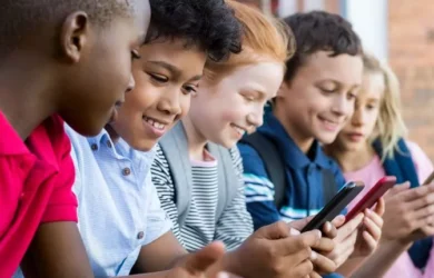 Children sit together using smartphones.